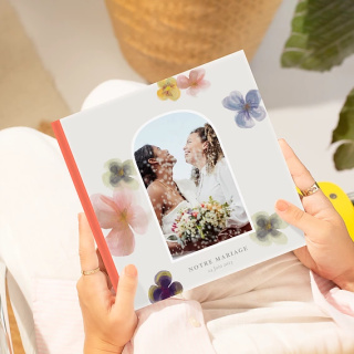 Album photo mariage fleuri tenu en main, couverture avec couple souriant et fleurs colorées